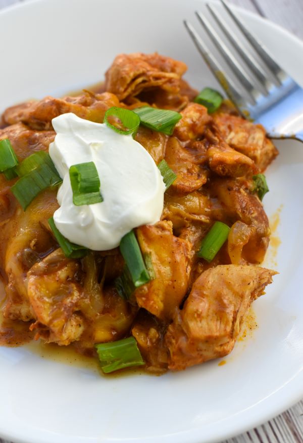 chicken enchilada casserole topped with green onions and sour cream on white plate