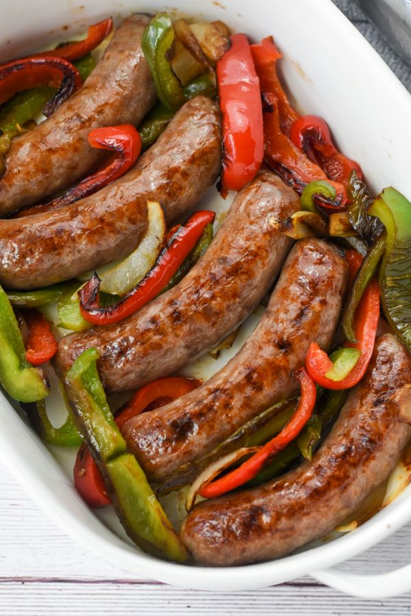 cooked brats in white casserole dish with peppers