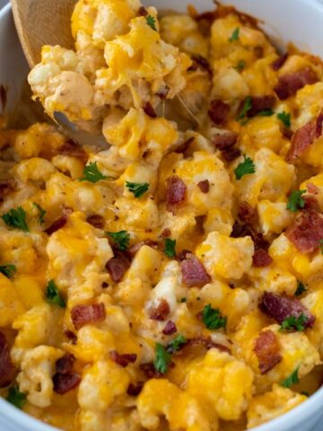 cauliflower mac and cheese topped with chopped bacon and parsley in white casserole dish