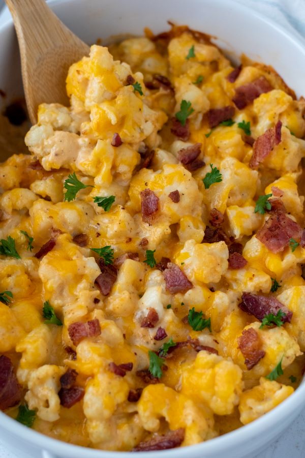 cauliflower mac and cheese topped with chopped bacon and parsley in white casserole dish