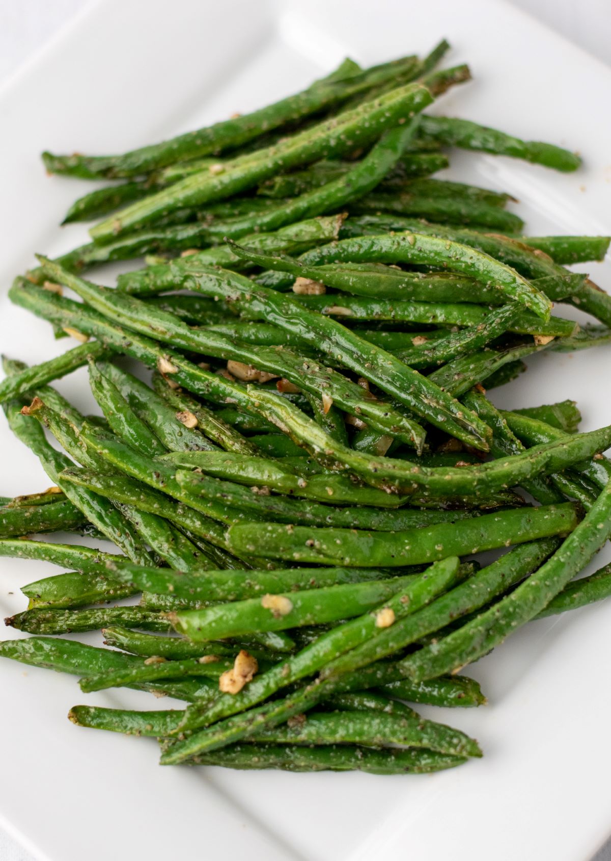 cooked green beans with minced garlic on white plate.