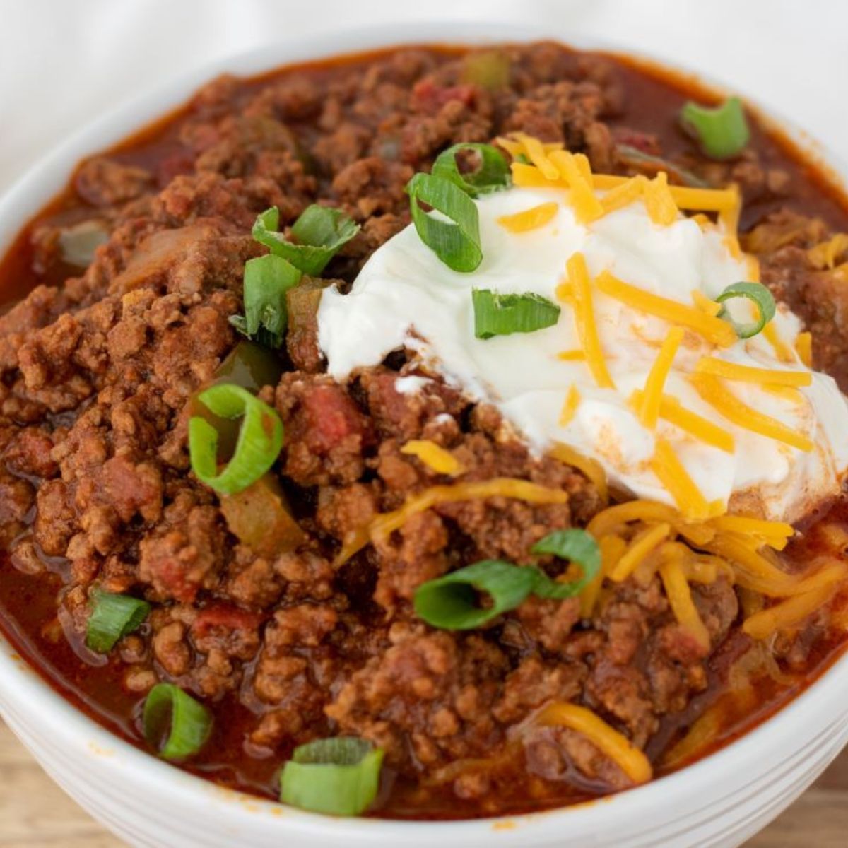 keto chili in white bowl topped with sour cream and shredded cheese